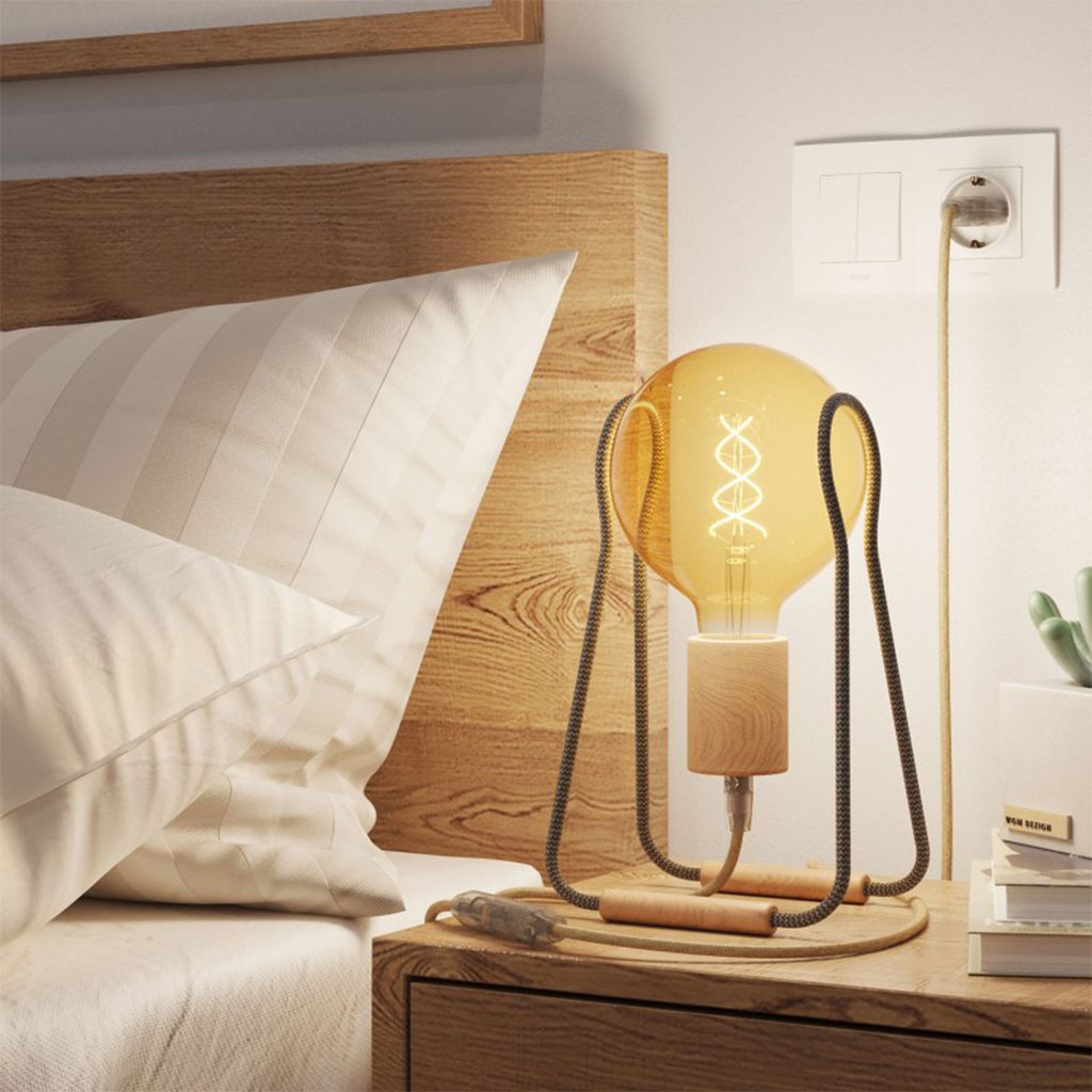 LED-Filament-Leuchtmittel mit sichtbarer Spiralstruktur in einer Holz-Tischleuchte am Bett