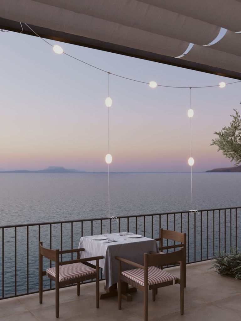 Tisch mit zwei Stühlen auf einer Terrasse mit Blick auf das Meer und hängenden Lichtern.