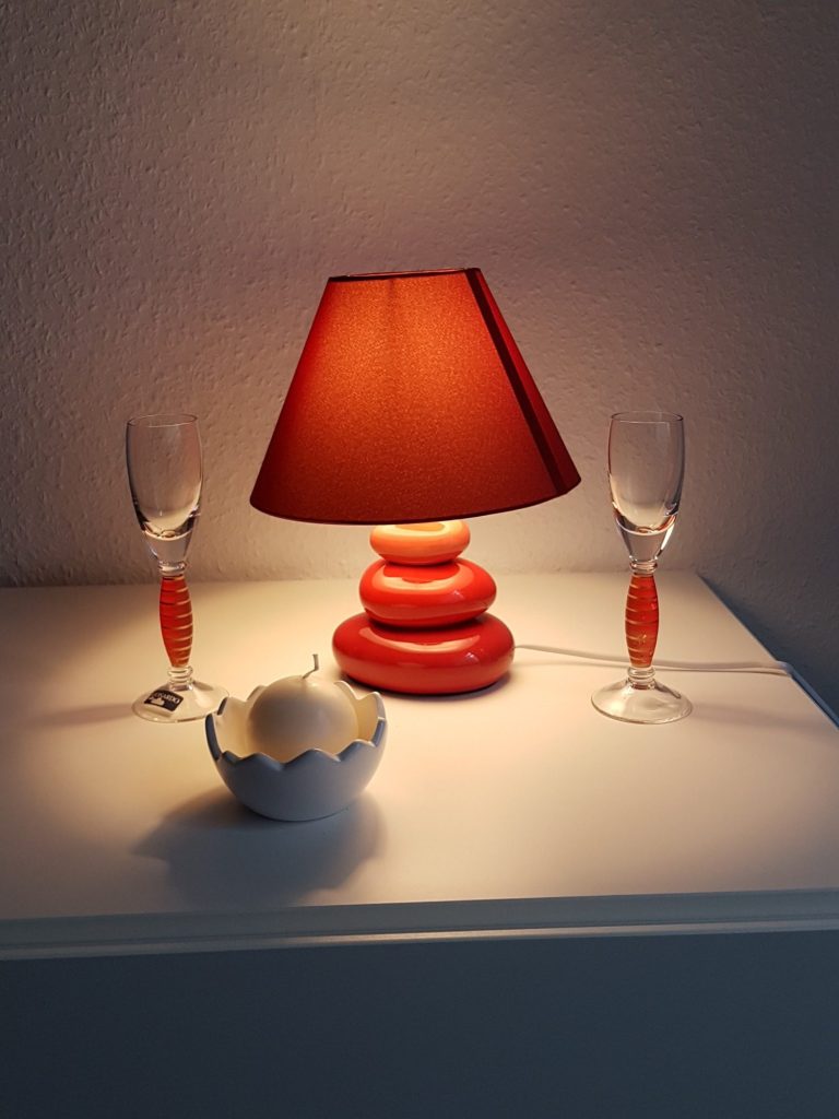 Rote Tischlampe mit zwei Gläsern und einer Schale auf einem weißen Tisch.