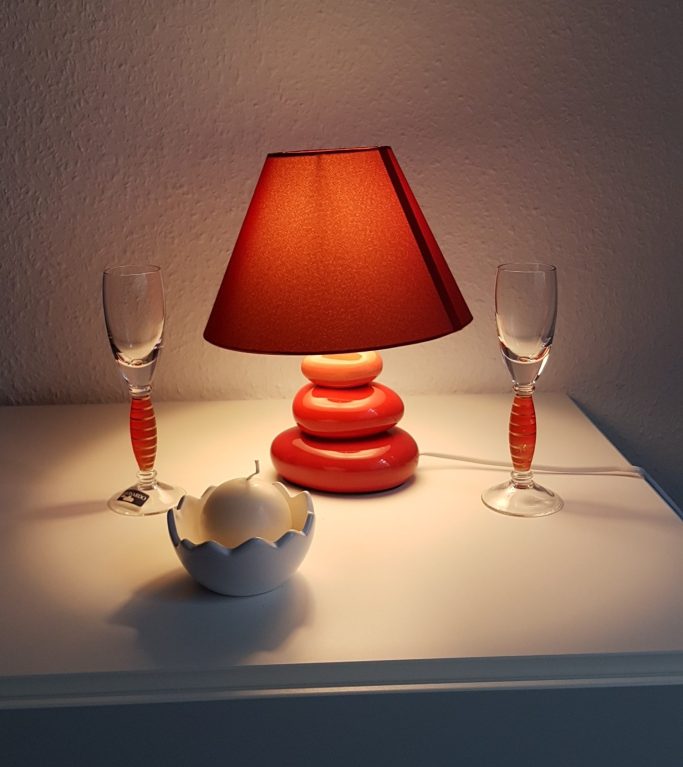 Rot lampenschirm mit weißen und orangen Dekorationsobjekten auf einem Tisch.