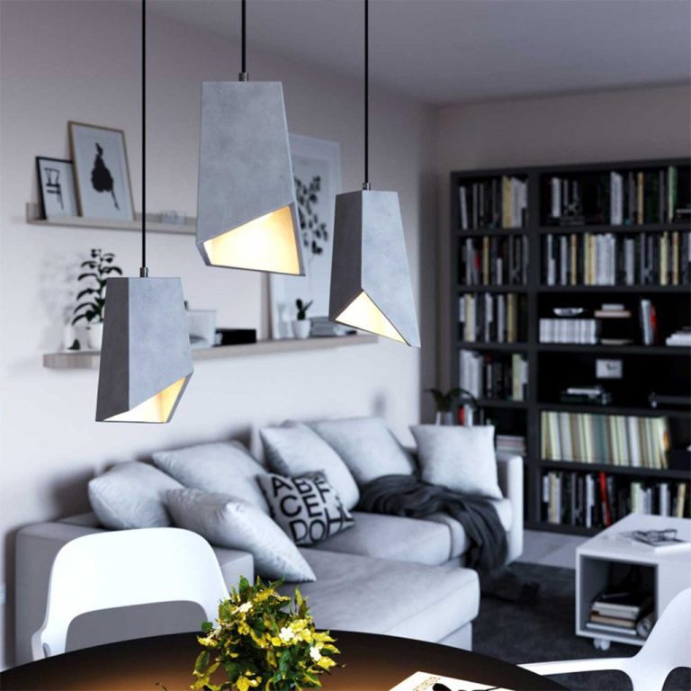 Moderne Betonlampen hängen über einem gemütlichen Wohnzimmer mit Sofa und Bücherregal.