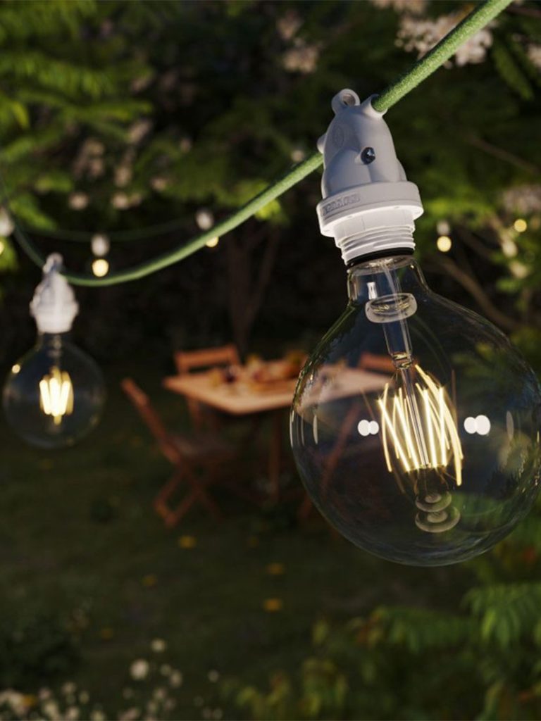 Hängende Glühbirnen auf einer Lichterkette in einem Gartensetting.