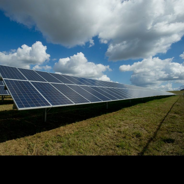 Solaranlage mit Photovoltaikmodulen auf einem Feld unter einem wolkigen Himmel.