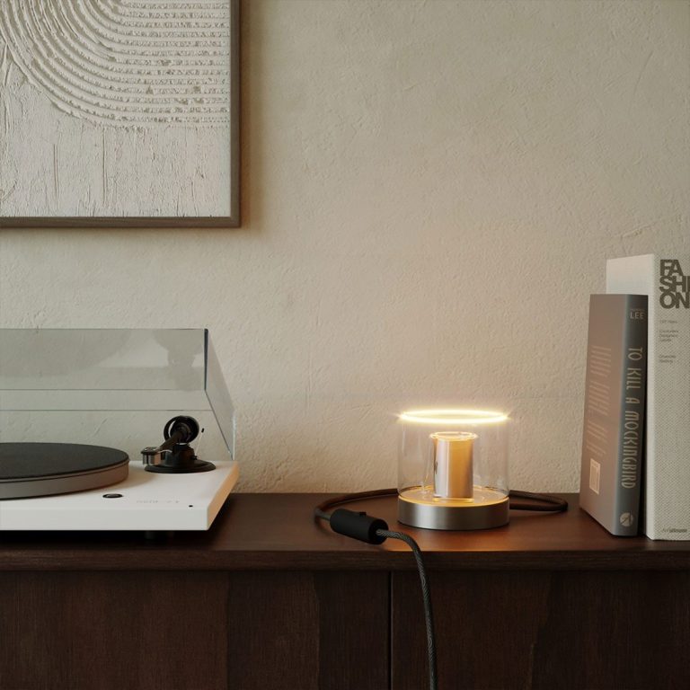 Ein Plattenspieler, eine Lampe und Bücher auf einem Holztisch in einem modernen Raum.