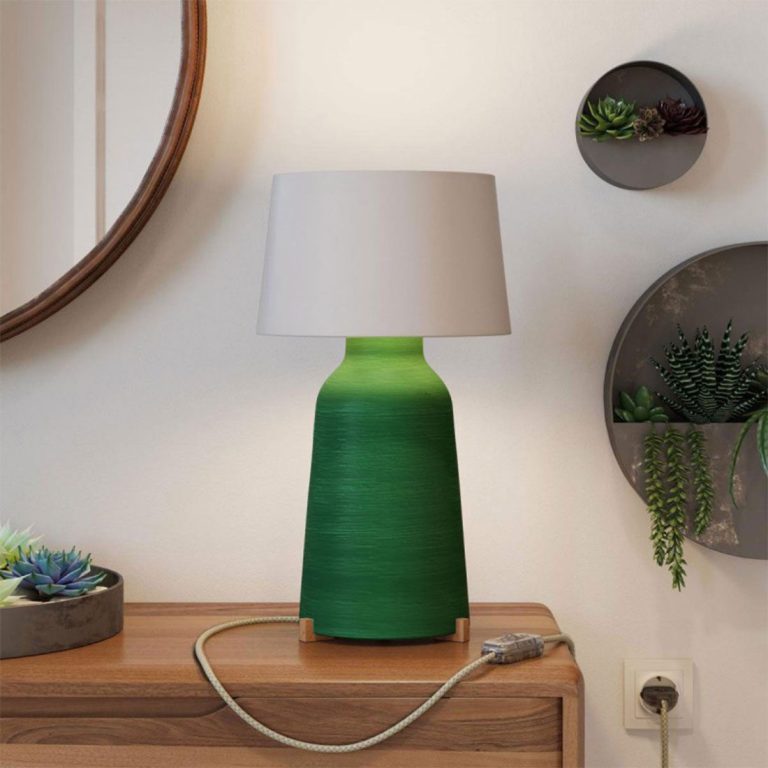 Grüne Tischlampe mit weißem Lampenschirm auf einem Holzsideboard.