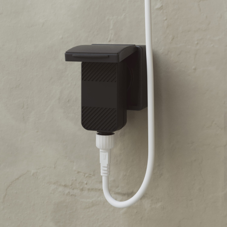 Schwarzer Stecker mit angeschlossenem weißen Kabel an einer grauen Wand.