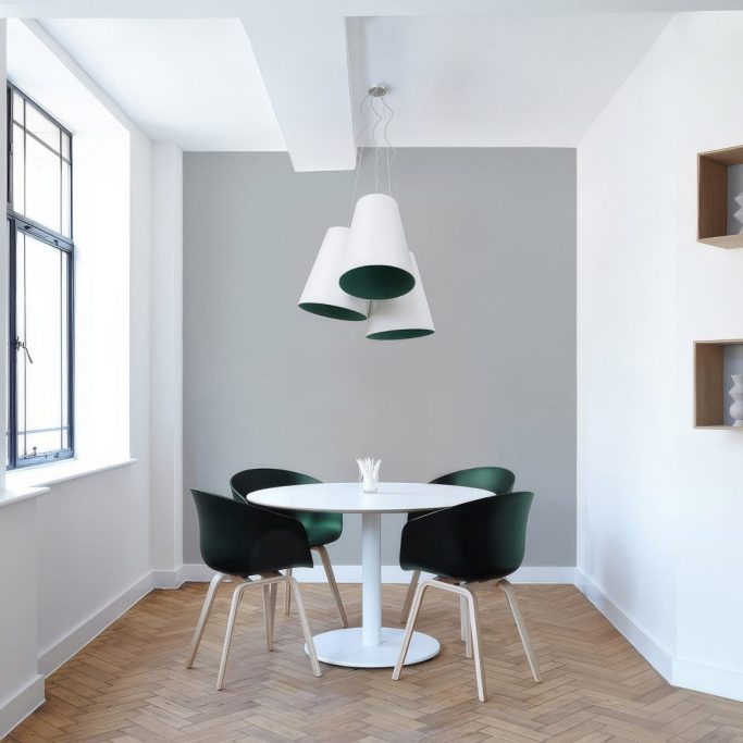 Modern Essbereich mit runden Tisch, grünen Stühlen und drei hängenden Lampen.