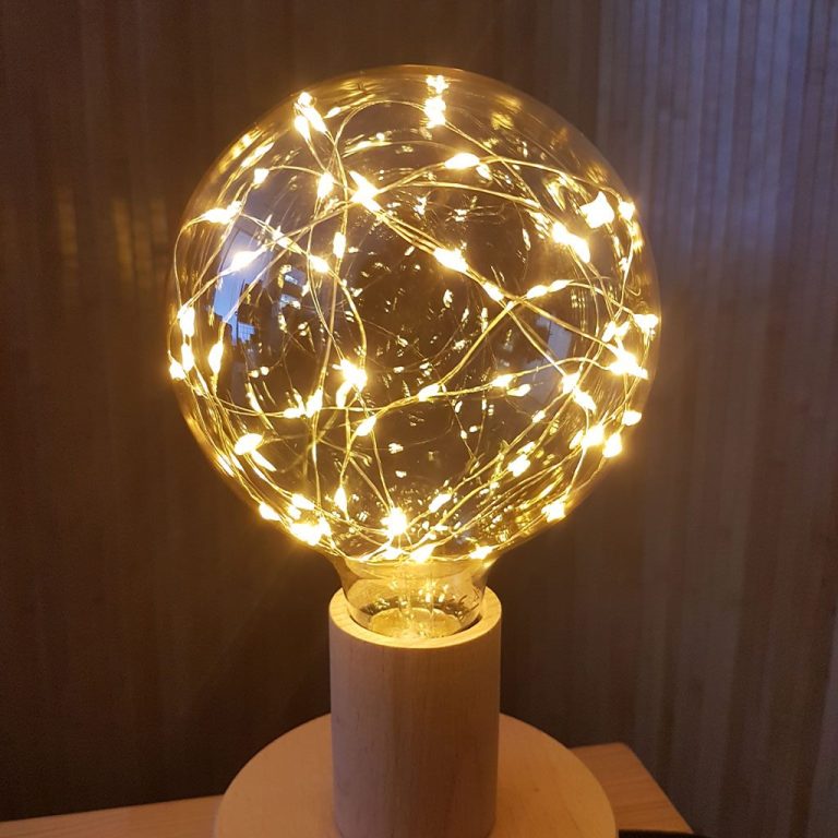 Glaskugel mit leuchtenden Lichtern und Holzsockel, warmes Ambiente.
