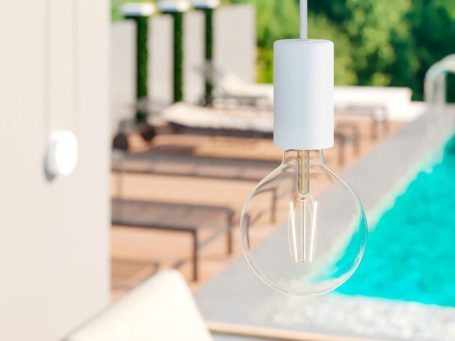 Einfache Glühbirne hängt über einem Poolbereich mit Liegen im Hintergrund.